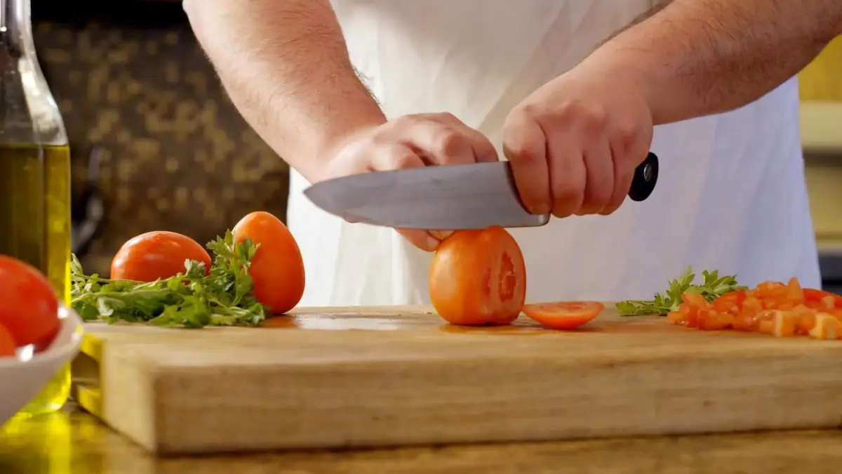 chef preper food cutting tomatoes on a wooden chopping board